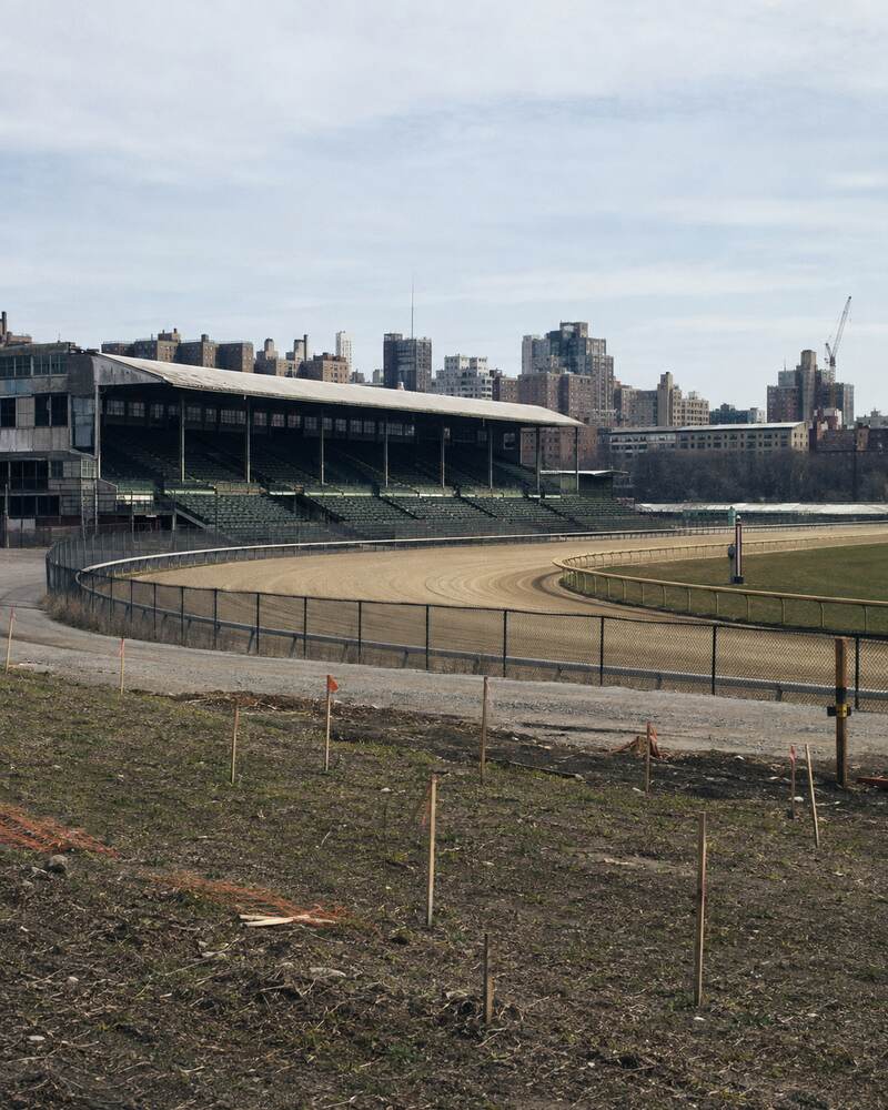 An empty urban racetrack and aging grandstand beside land marked for future planning.