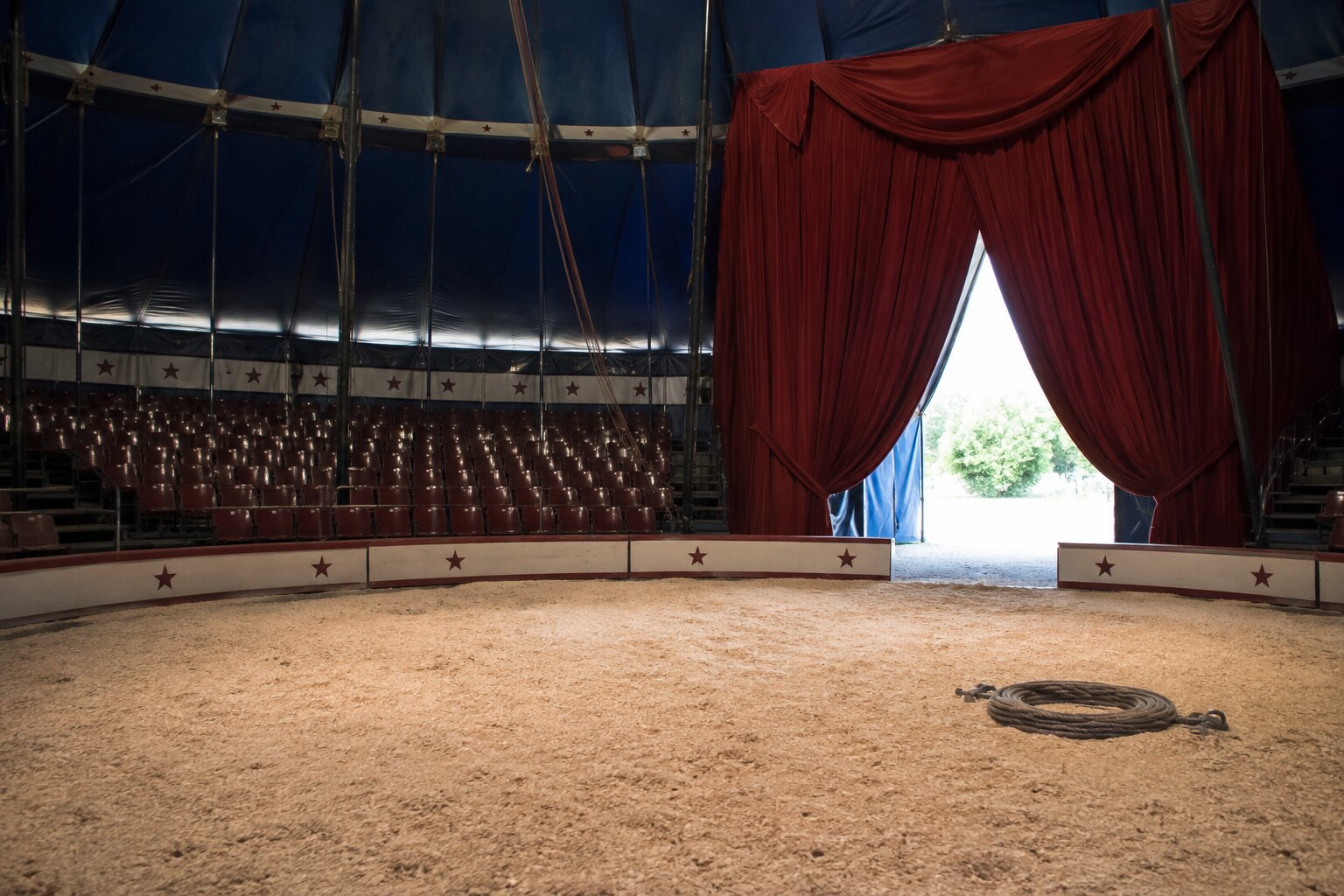 An empty traveling circus ring with an open exit and a coiled tether on the floor